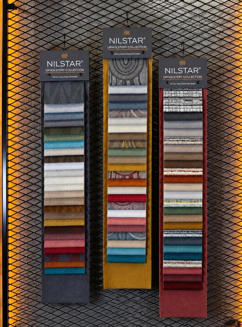 Three Nilstar Upholstery Collection swatch books displayed on a showroom panel